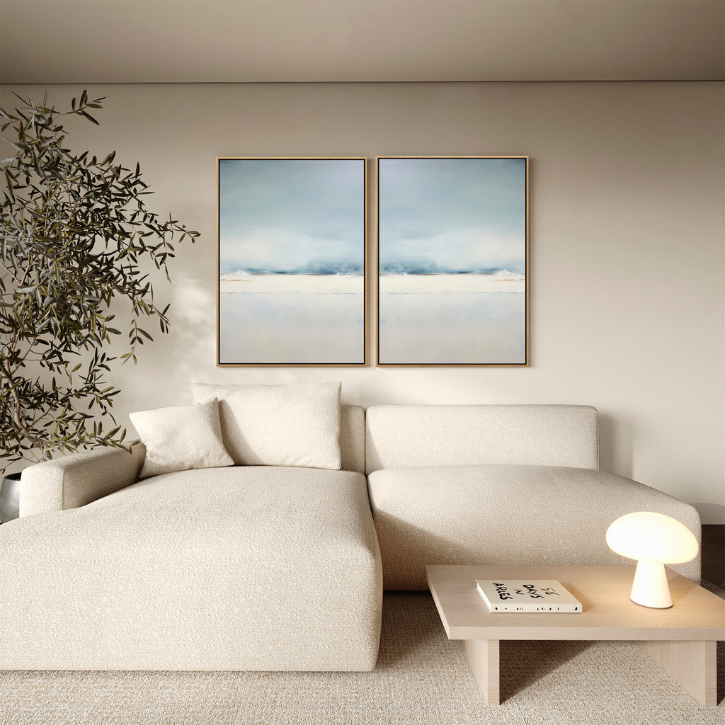 A modern living room featuring a cream sectional, a small wooden coffee table with a lamp and book, a tall leafy plant, and the Misty Morning Set of 2 minimalist wall art, creating a tranquil atmosphere.