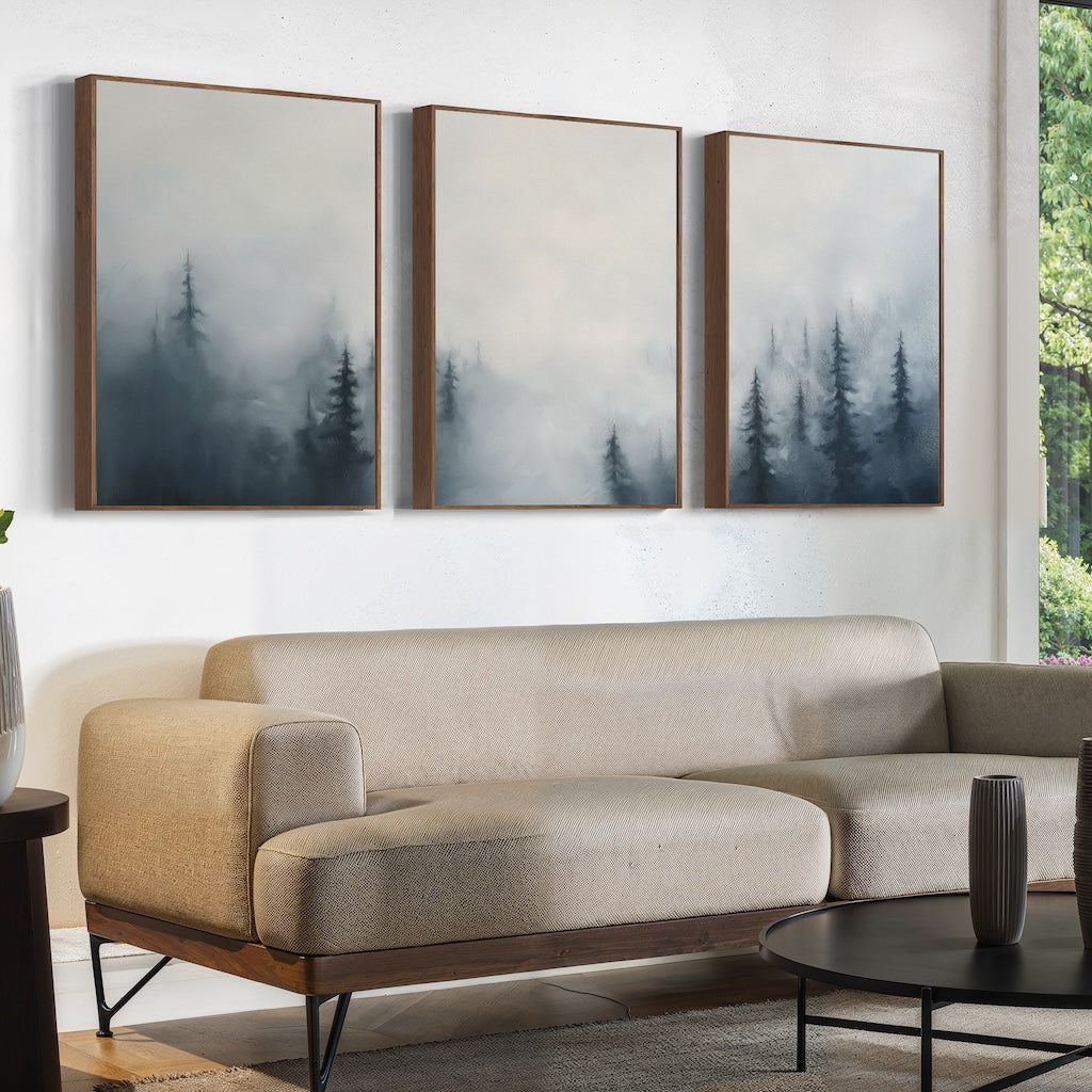 A modern living room with a beige sectional, a round black coffee table, and the Misty Pines Set of 3 wall art above the sofa. Lush greenery is framed by the window, creating a calming Nordic Park atmosphere.