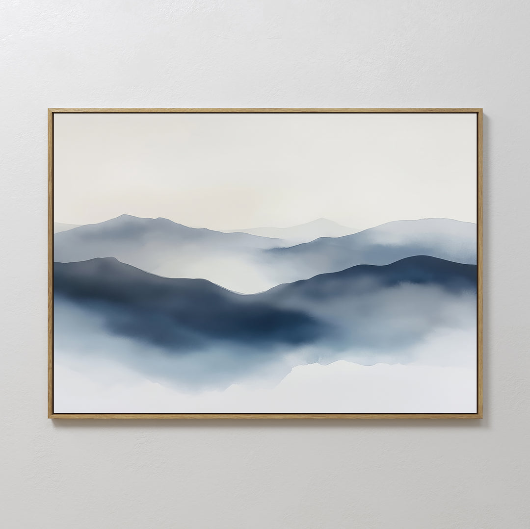 The Misty Ridge Canvas Art – Horizontal features a minimalist landscape of layered blue and gray mountains fading into the distance under a soft white sky, displayed in a thin light-colored frame on a plain white wall.