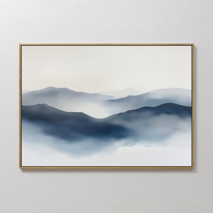 The Misty Ridge Canvas Art – Horizontal features a minimalist landscape of layered blue and gray mountains fading into the distance under a soft white sky, displayed in a thin light-colored frame on a plain white wall.