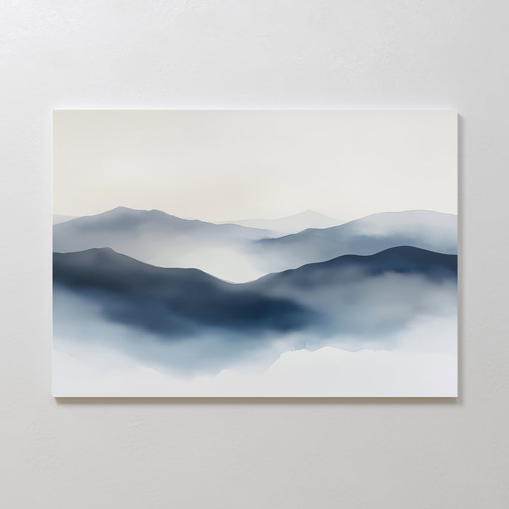 The Misty Ridge Canvas Art – Horizontal features a minimalist landscape of layered blue and gray misty mountains with soft gradients and blurred edges, creating a serene atmosphere. This abstract wall art is displayed on a plain white wall.