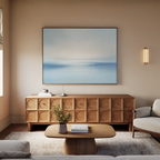 A modern living room features a light wood coffee table, textured wood sideboard, beige sofa, and Misty Waters Canvas Art above. A small plant and minimalist accents decorate the space, gently illuminated by soft natural light.
