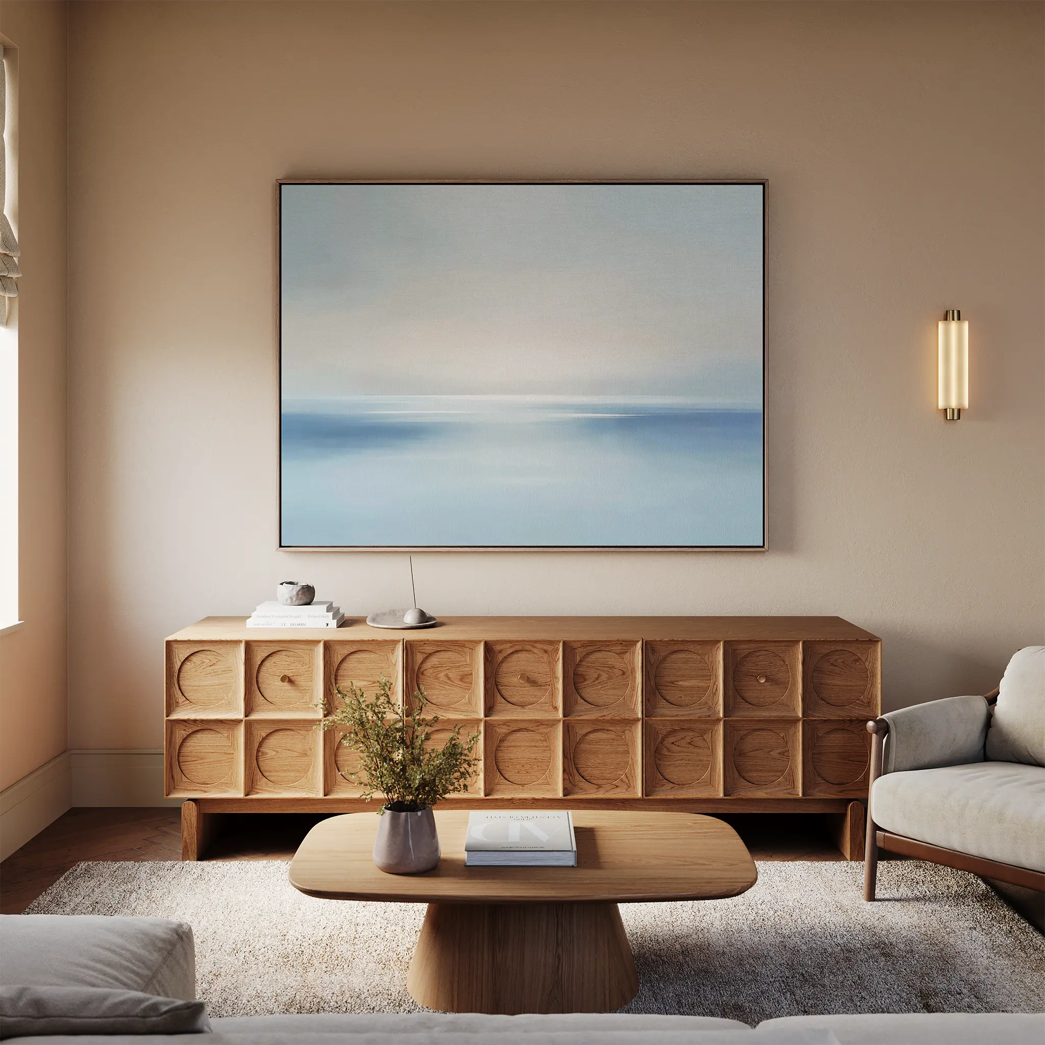 A modern living room features a light wood coffee table, textured wood sideboard, beige sofa, and Misty Waters Canvas Art above. A small plant and minimalist accents decorate the space, gently illuminated by soft natural light.