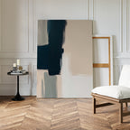Modern Contrast Abstract Canvas Art leans against a white paneled wall near an empty frame, with a small round table holding candles and books beside a white cushioned chair on a herringbone wood floor—ideal minimalist wall decor.