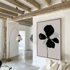 A modern living room features exposed wooden beams, white walls, a light sofa with cushions, a curved floor lamp, and the Monochrome Flora Abstract Canvas Art as minimalist wall decor. Natural light brightens the space.