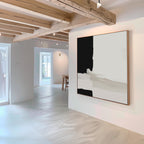 A bright, minimalist room with exposed wooden beams and white walls features Monochrome Harmony Abstract Canvas Art as the centerpiece. Sunlight pours in through windows, with a glimpse of a table seen in the background.