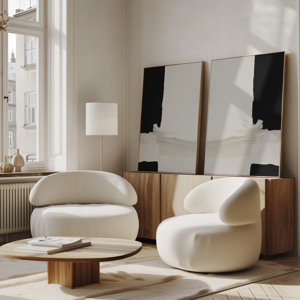 A modern living room features the Monochrome Harmony Set of 2 curved white armchairs, a round wooden coffee table, a wooden sideboard, and bold black and white wall art. Large windows fill the sunlit space with natural light.