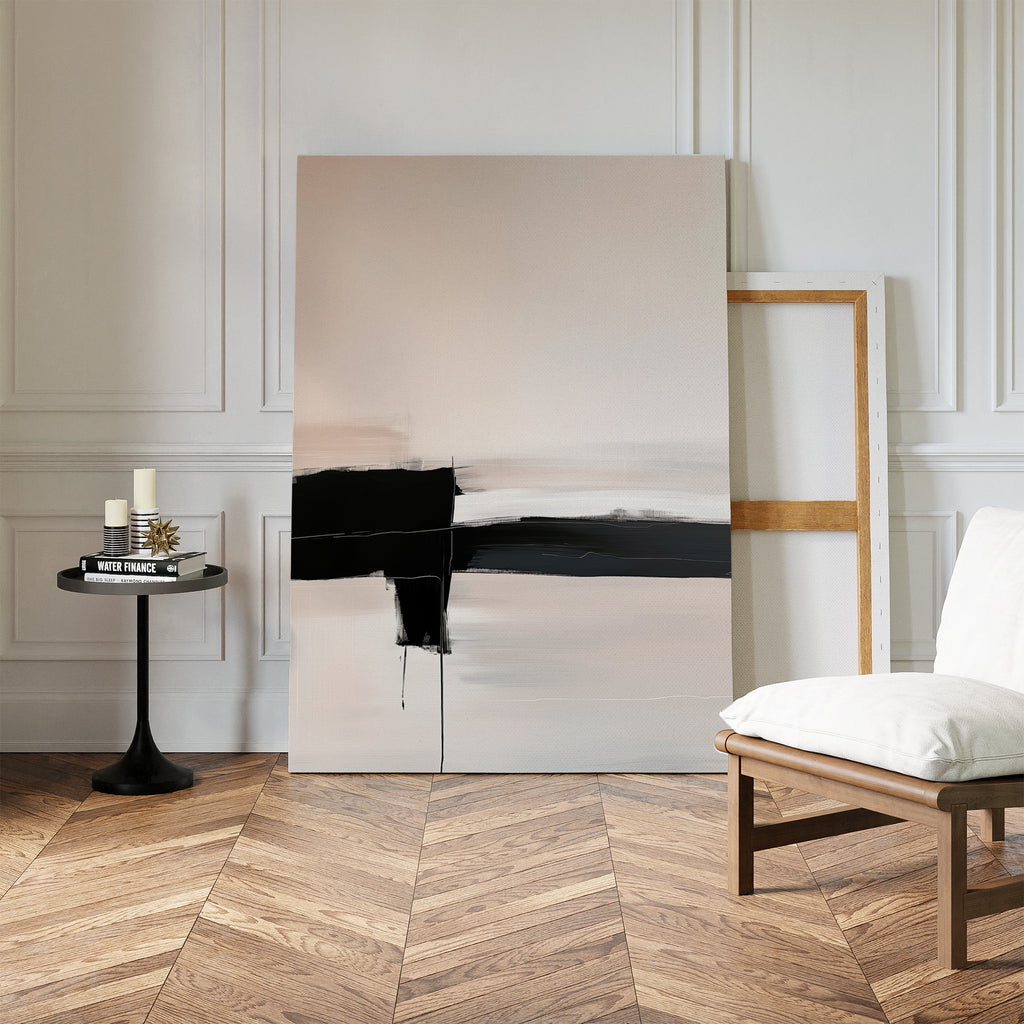 A modern minimalist room features the Monochrome Horizon Abstract Canvas Art with bold black brushstrokes leaning against the wall, a small round table with candles and books, and a white cushioned chair on herringbone wood flooring.