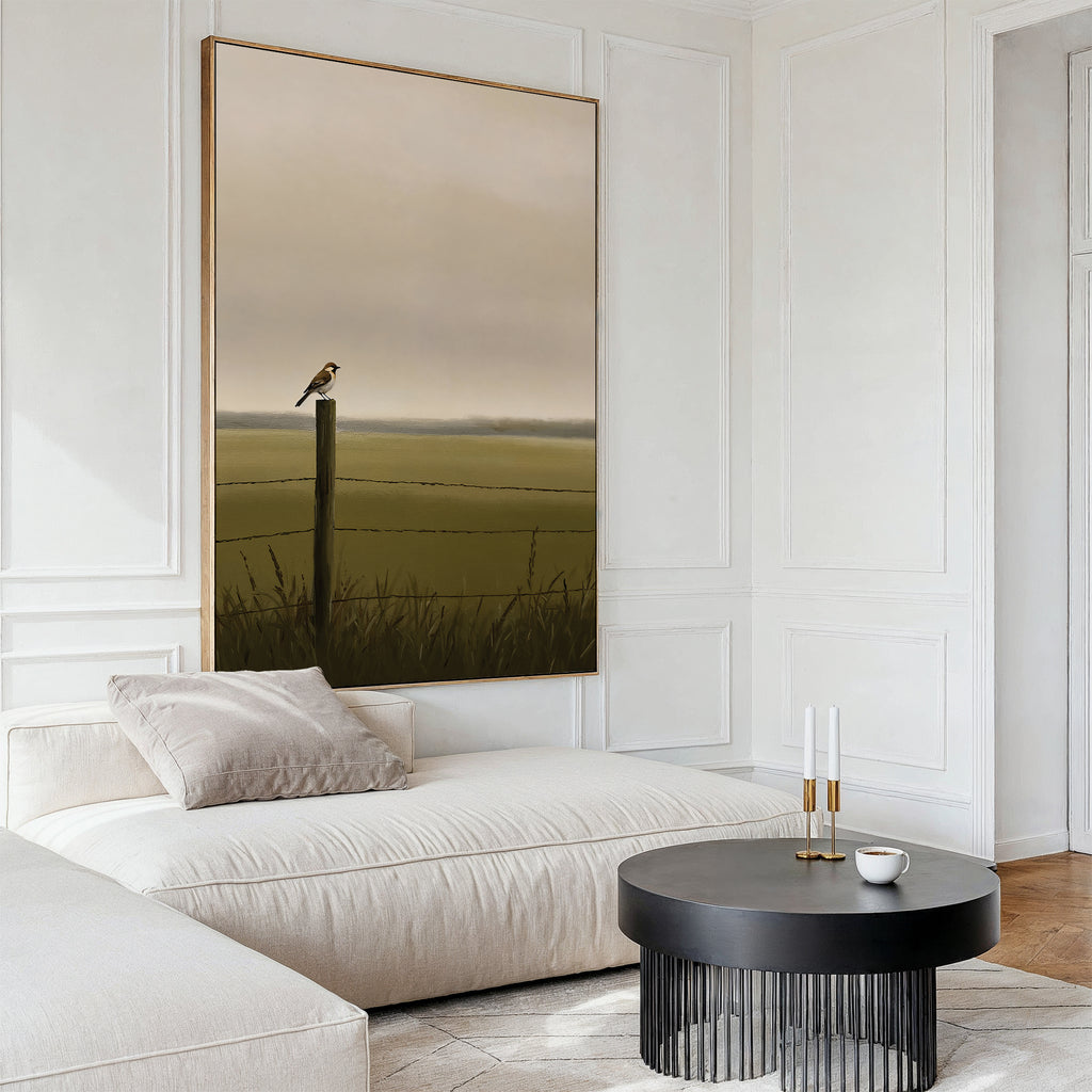 A modern living room with a beige sectional, round black coffee table, and the Morning Perch Canvas Art featuring a bird on a fencepost in a misty green field. Minimalist decor and neutral tones complete the earthy interior.