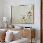 A light, minimalist living room features a wooden sideboard, a white table lamp, stacked books, a bowl, and the Morning Petals Canvas Art above the sideboard. A cream sofa in the foreground completes the serene atmosphere.