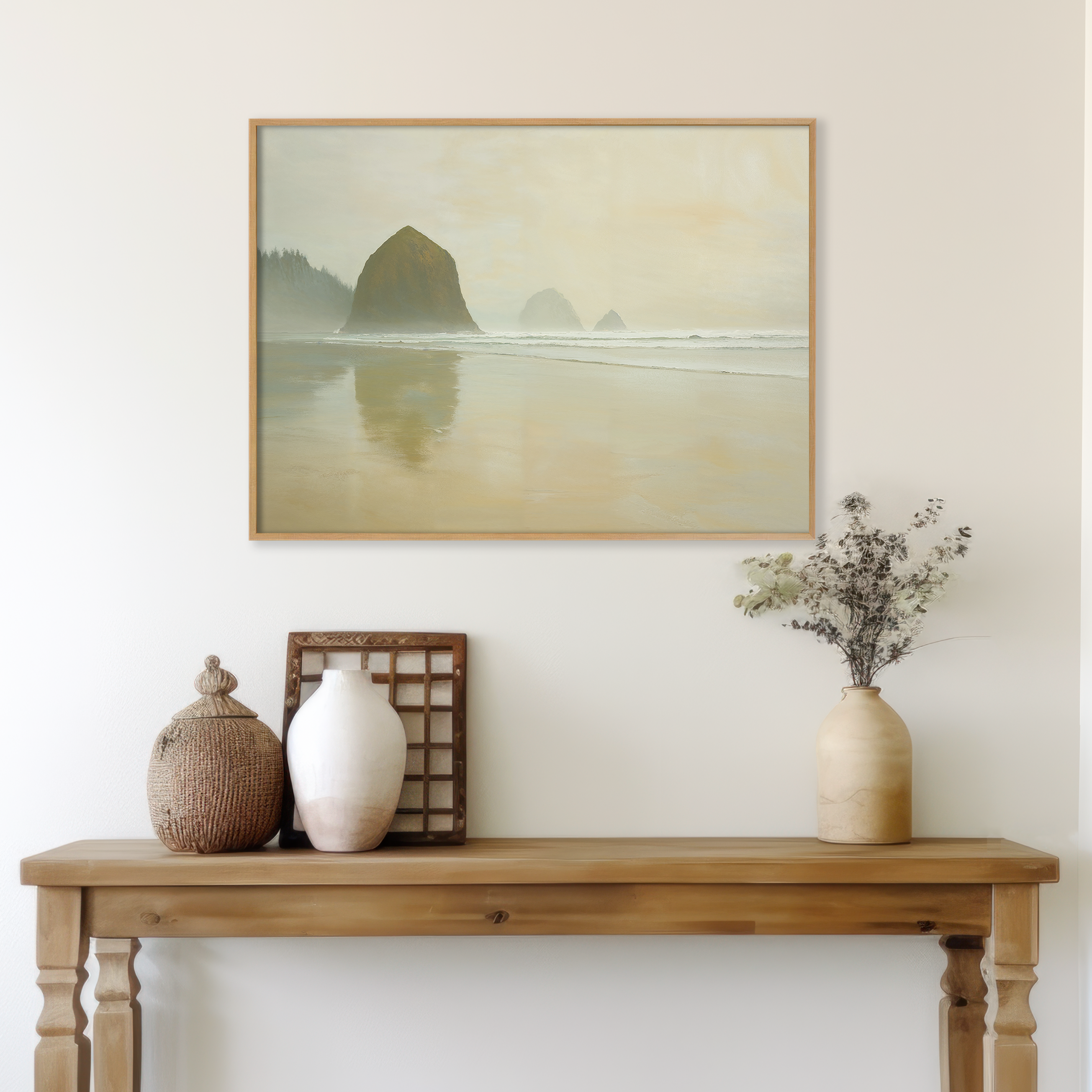 A minimalist wooden table with vases, a basket, and dried flowers sits below a light wall featuring Morning At Cannon Beach Canvas Art, showcasing sea stacks and misty waves for a calm, coastal vibe.