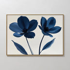 Navy Flora Canvas Art showcases two large blue flowers with dark centers and elongated leaves on a white background, set in a slim gold frame—ideal for adding striking minimalist style to your wall decor.