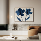 A modern living room with neutral tones showcases the Navy Flora Canvas Art—a minimalist print of two blue flowers—above a marble shelf with dried flowers and candles. A curved tan sofa is placed in the foreground.