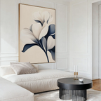 A minimal, modern living room featuring Navy Magnolia Canvas Art, a beige sectional with neutral pillows, a round black coffee table with candles and a white teacup on a saucer. White paneled walls complete the decor.