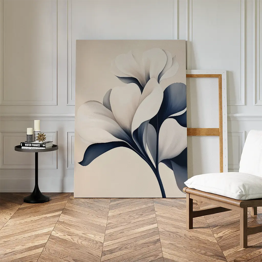 The Navy Magnolia Canvas Art, a large abstract floral piece in white and navy, leans against a paneled wall beside a framed canvas, chair with cushion, and table with candles—perfect for modern living room decor.