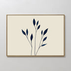 Navy Stem Canvas Art features thin black stems with solid navy blue leaves on a beige background, framed in slim wood and displayed on a white wall for striking, modern minimalist decor.
