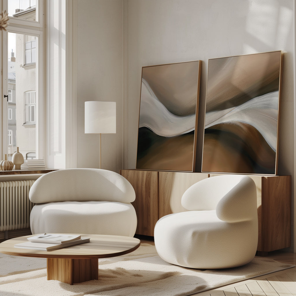 A modern living room features two curved white armchairs, a low wood coffee table, a tall floor lamp, and the Neutral Landscape River Set of 2 wall art on a wooden sideboard by a large window—perfect for stylish decor.