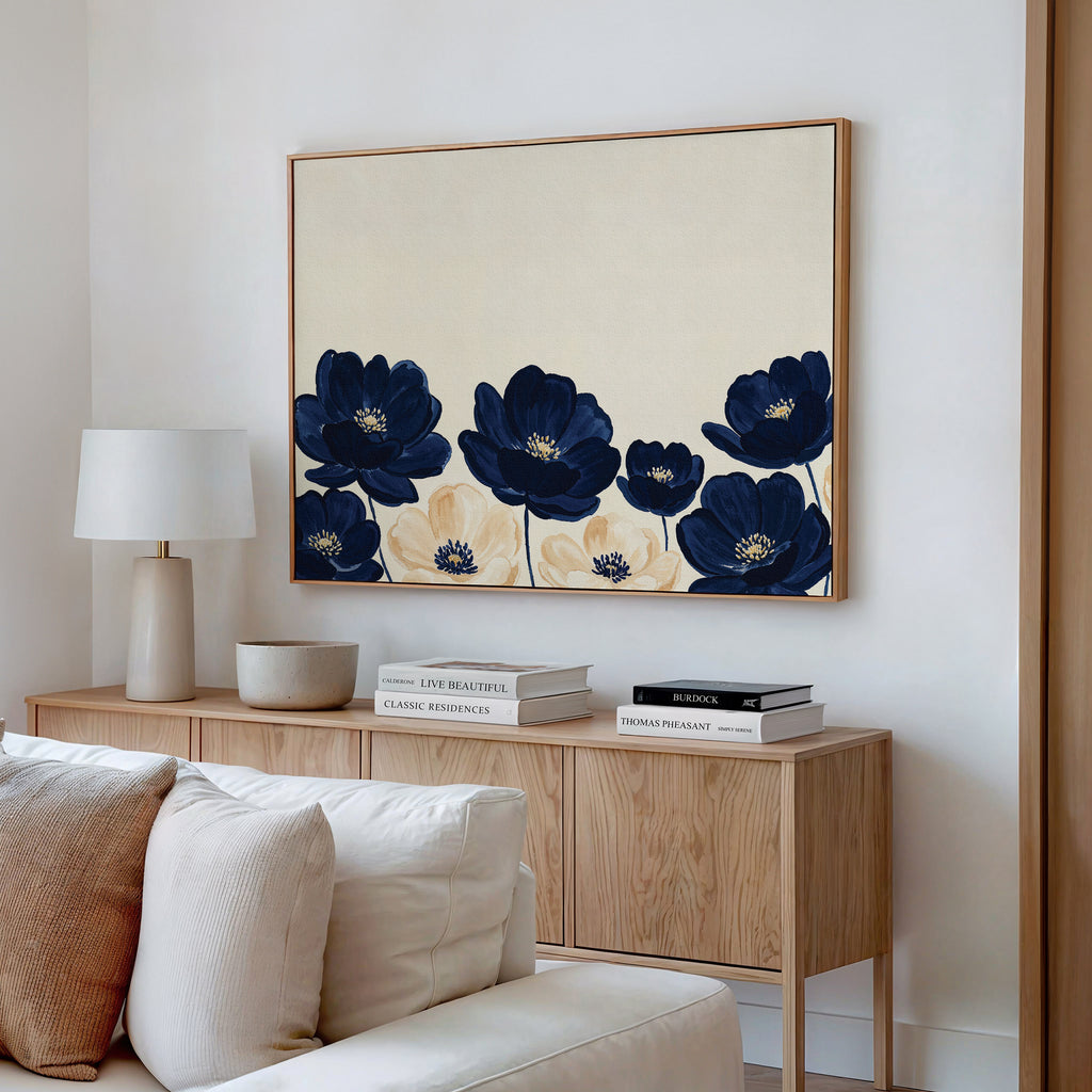 A modern living room features a light wood sideboard with a lamp, decor, and books. Above it hangs the Nightshade Canvas Art – Horizontal in navy and beige. A cream sofa appears in the foreground.