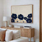 A modern living room features a light wood sideboard with a lamp, decor, and books. Above it hangs the Nightshade Canvas Art – Horizontal in navy and beige. A cream sofa appears in the foreground.