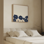 A modern bedroom with a beige bed, white pillows, and the Nightshade Canvas Art—a large framed piece featuring dark blue and beige flowers on a neutral background—displayed above the headboard.