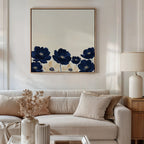 A cozy living room features a beige sofa with neutral pillows, a lamp on a wooden side table, and the Nightshade Canvas Art—modern wall art with blue flowers—above the sofa. Dried flowers in a vase adorn the coffee table.