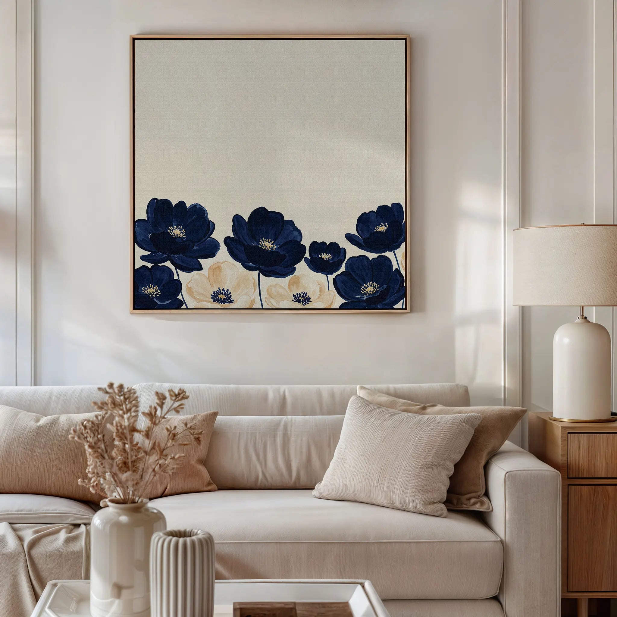 A cozy living room features a beige sofa with neutral pillows, a lamp on a wooden side table, and the Nightshade Canvas Art—modern wall art with blue flowers—above the sofa. Dried flowers in a vase adorn the coffee table.