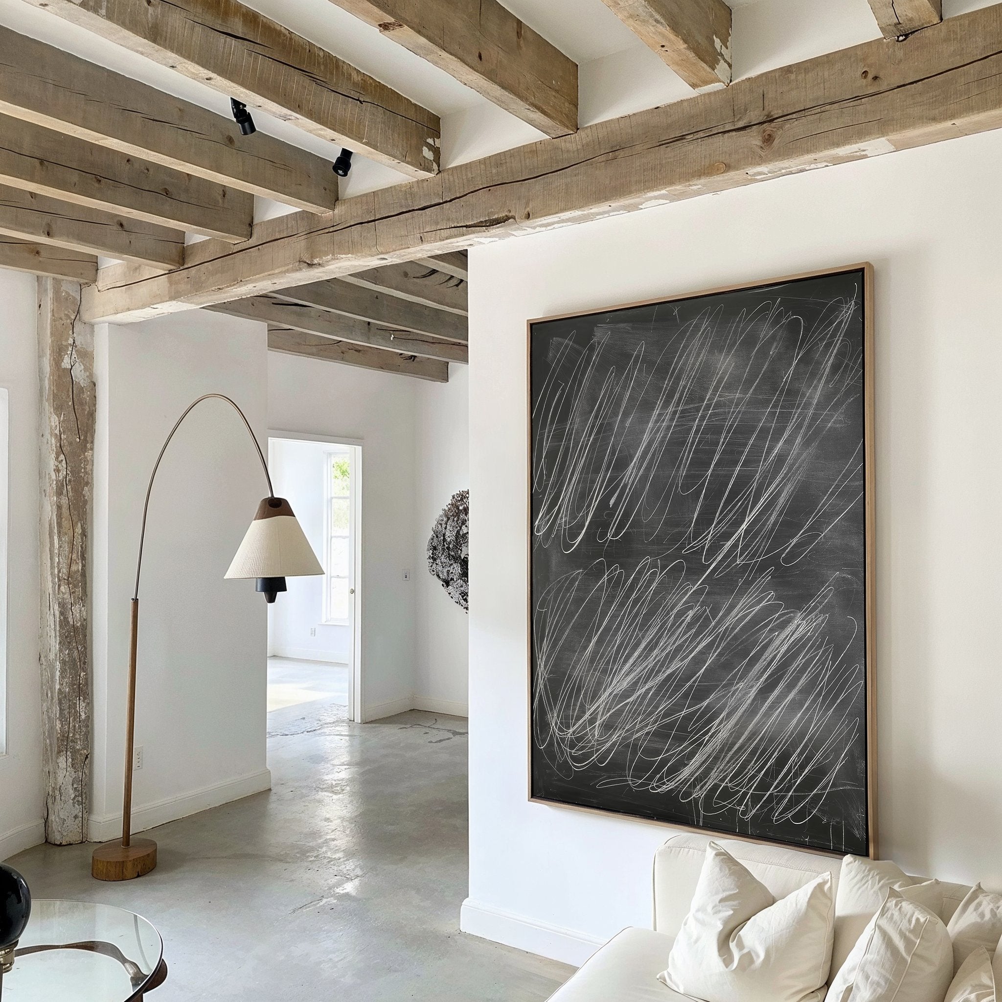 A modern living room with exposed wooden beams, white walls, a white couch with pillows, a curved floor lamp, and Echoes in Chalk Abstract Canvas Art featuring white scribbles as the focal wall decor.