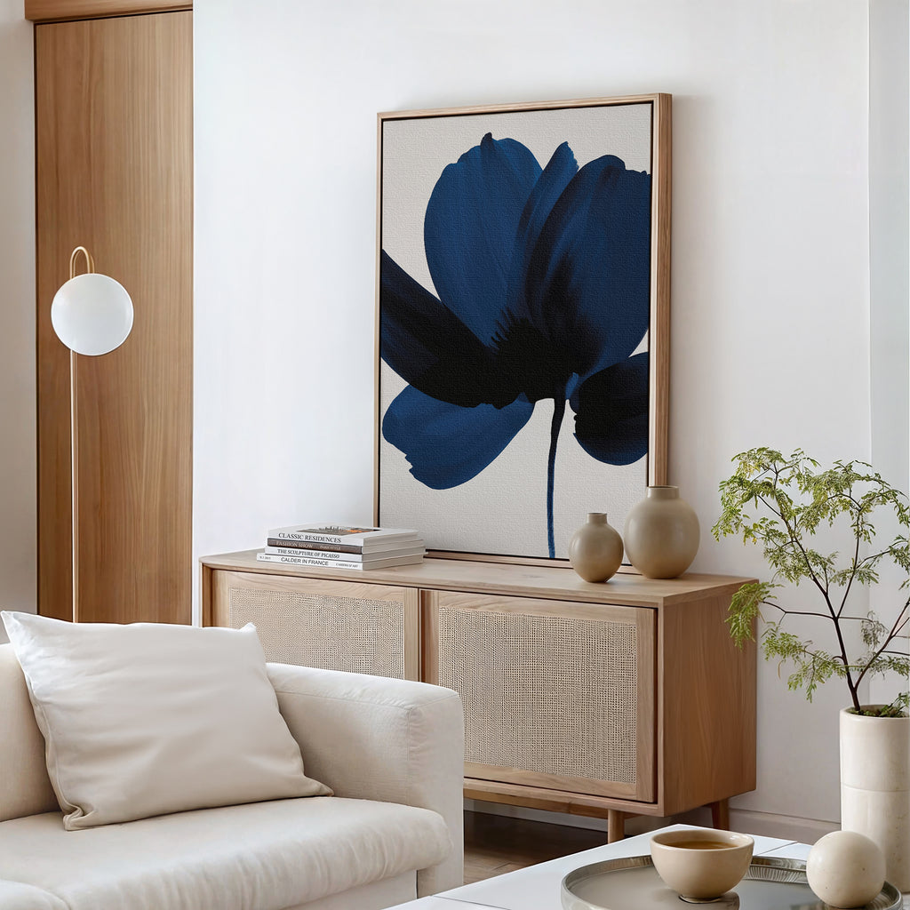 A modern living room features a wooden sideboard, the Nocturne Blossom Canvas Art with blue florals, decorative vases, stacked books, a potted plant, a round white lamp, and a beige sofa with white cushions for chic decor.