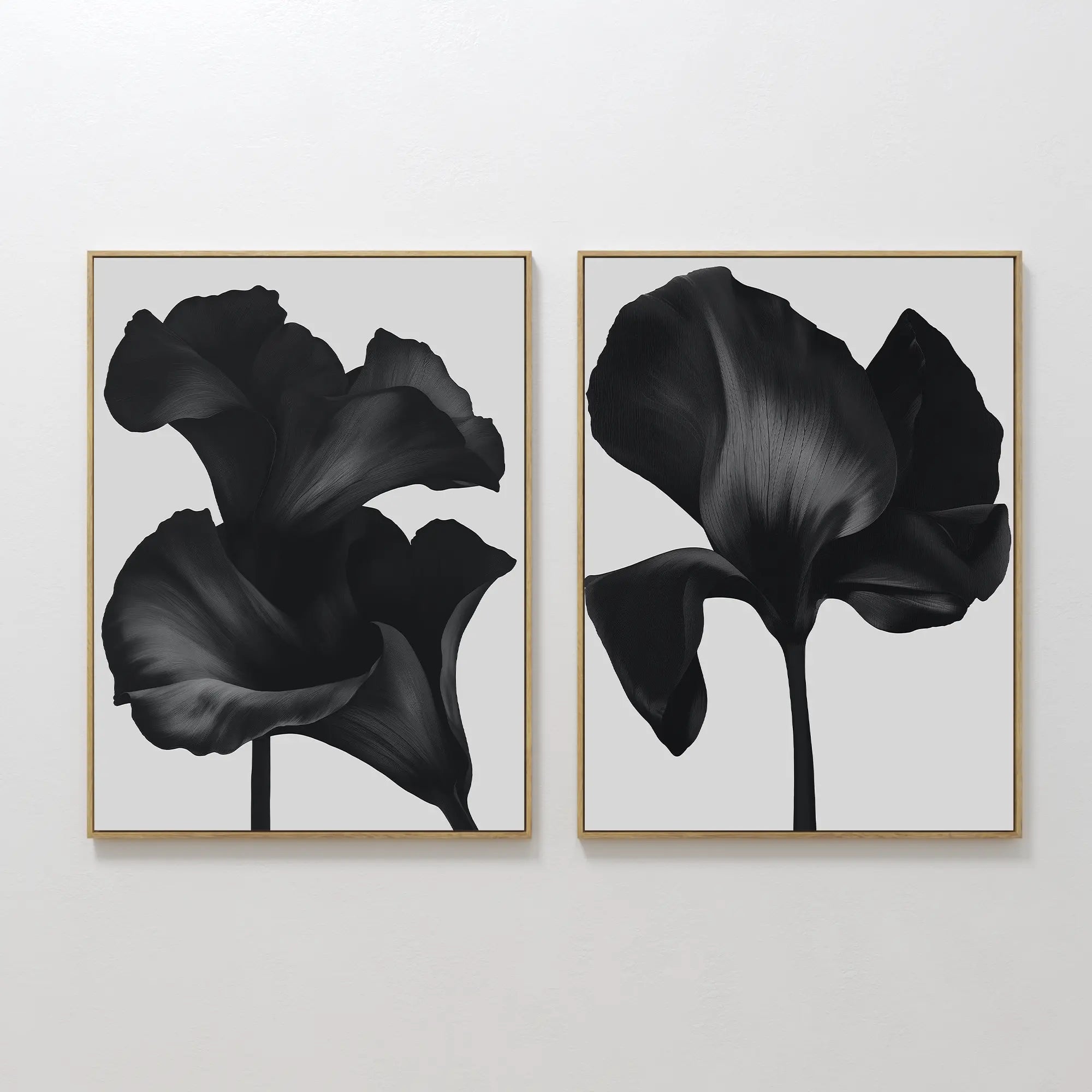 The Noir Bloom Set of 2 features framed wall art prints with black flower silhouettes on light gray, each showing a different broad-petaled bloom in a minimalist, contemporary style, hung side by side on a plain white wall.
