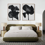 A modern bedroom featuring a green upholstered bed with white bedding, two beige bedside tables and matching lamps, and the Noir Bloom Set of 2 black floral prints displayed above the bed.