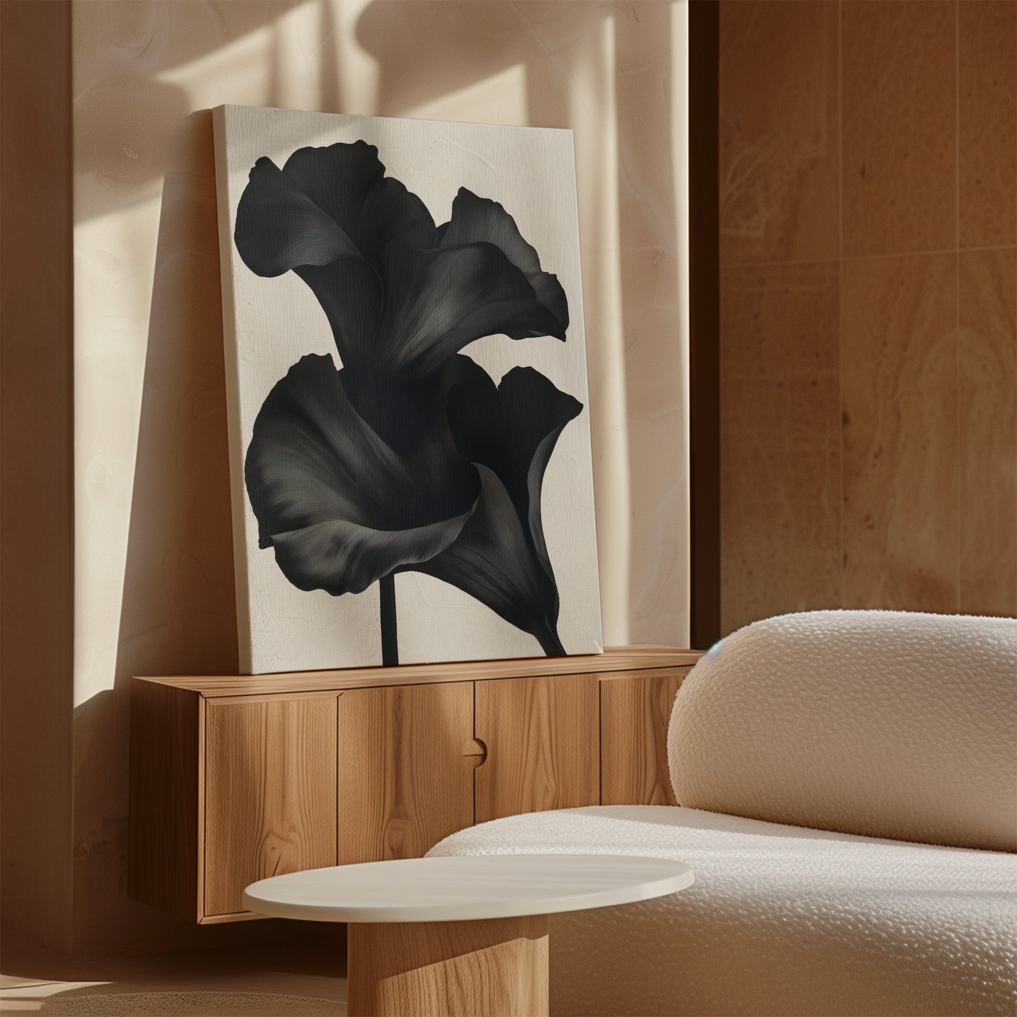 A minimalist room features a wooden sideboard topped with Noir Bloom Abstract Canvas Art—a large black and white floral painting—beside a textured white sofa and round coffee table, all softly illuminated by natural sunlight.