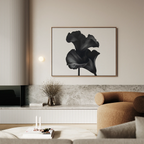 A modern living room with a beige armchair, a low marble shelf, dried flowers in a vase, and the Noir Bloom Canvas Art – Horizontal featuring bold black and white florals on a neutral wall—perfect for stylish decor.