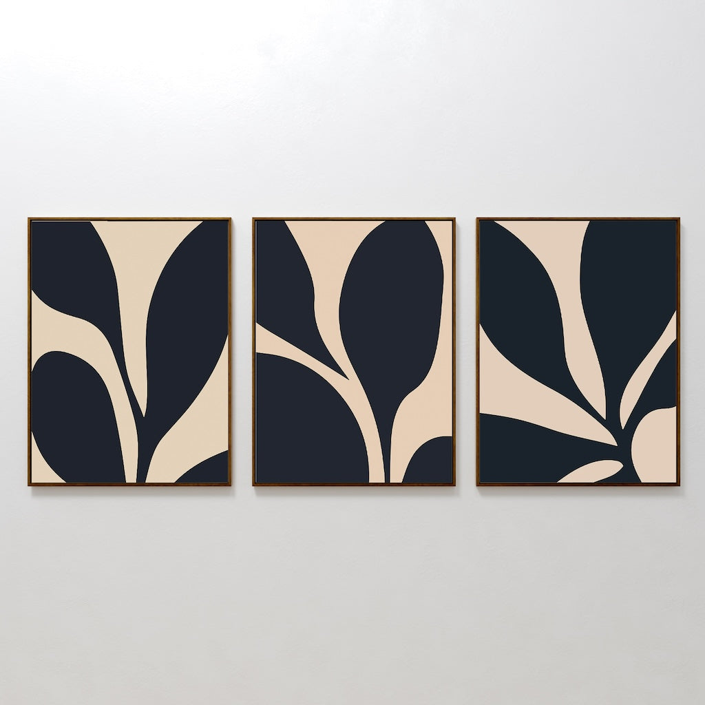 The Noir Blossom Set of 3 features bold, minimalist abstract art prints with black and beige leaf-like shapes in wooden frames, displayed side by side on a white wall for a seamless, modern look.