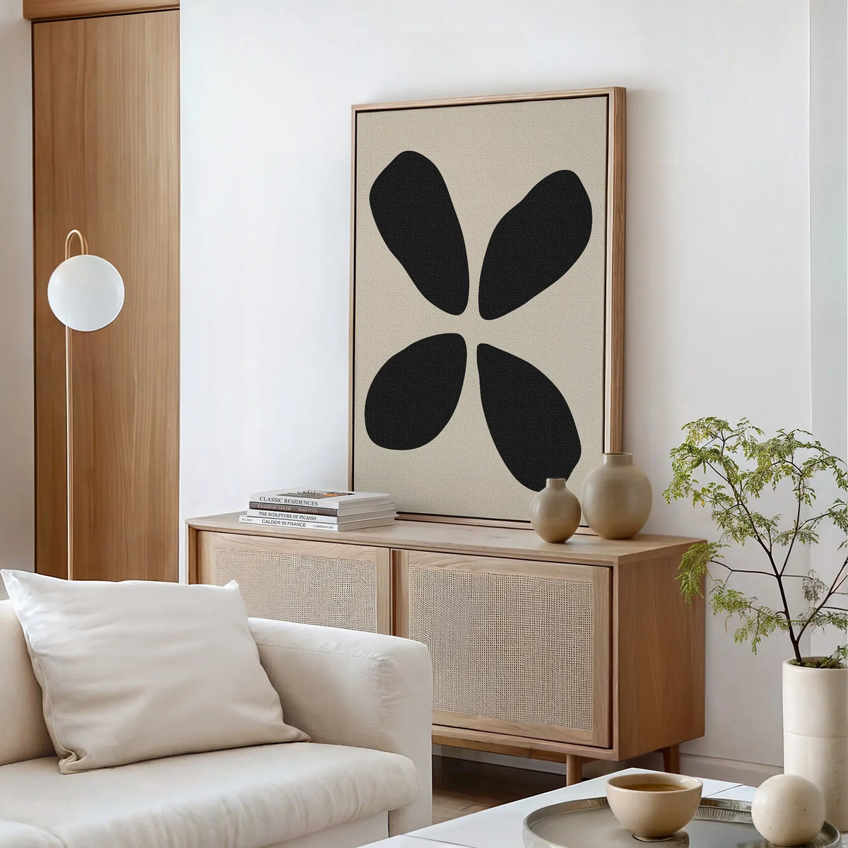 A modern living room with light wood furniture, a white sofa, a round coffee table, and the Noir Botanica Canvas Art above the sideboard. A potted plant and neutral-toned decor complete the sophisticated look.