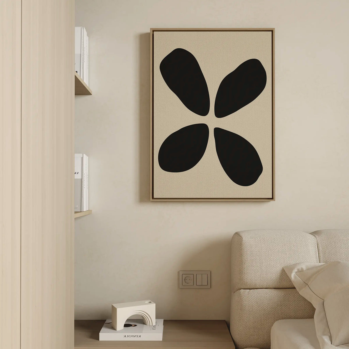 Minimalist living room with a beige couch, neutral walls, and the Noir Botanica Canvas Art—an abstract piece with four bold black shapes. Modern decor like a small shelf with books and a geometric sculpture complete the clean aesthetic.