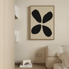 Minimalist living room with a beige couch, neutral walls, and the Noir Botanica Canvas Art—an abstract piece with four bold black shapes. Modern decor like a small shelf with books and a geometric sculpture complete the clean aesthetic.
