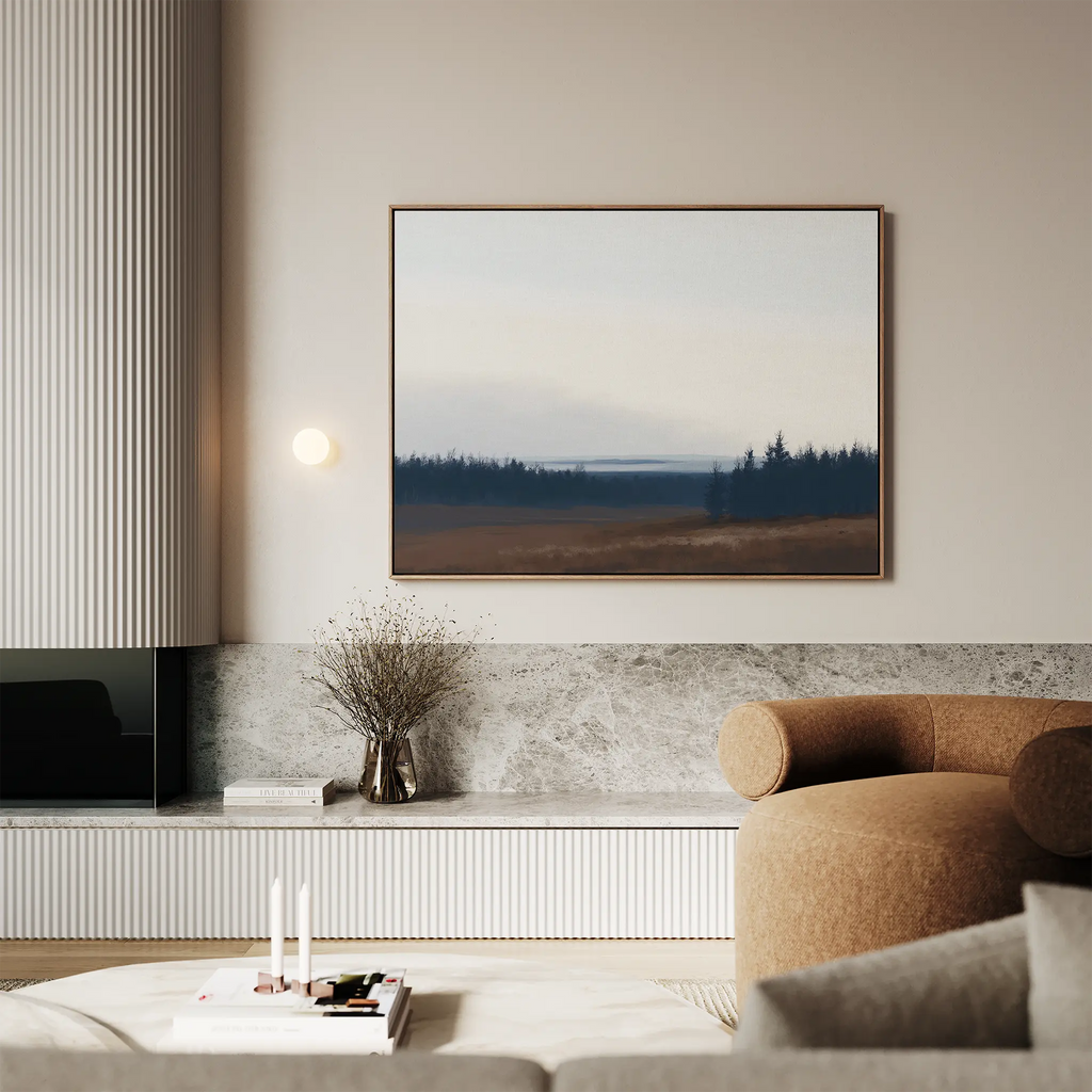 A modern living room with neutral tones features Northern Woods Canvas Art above a marble shelf, a round brown armchair, and minimalist decor including a vase with dried branches.