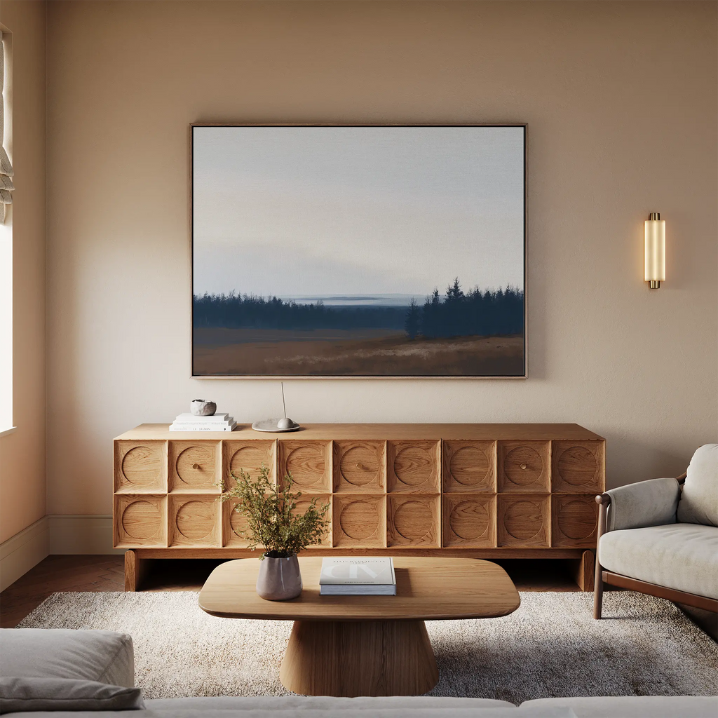 A cozy living room with a modern wooden sideboard, minimalist coffee table, light sofa, beige walls, and the Northern Woods Canvas Art above the sideboard. A small vase with flowers sits on the table.