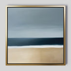 Ocean Edge Canvas Art features minimalist coastal wall art with a sandy beach, dark blue sea, and cloudy sky in soft, blended tones. Elegantly presented in a sleek gold frame for a modern touch.