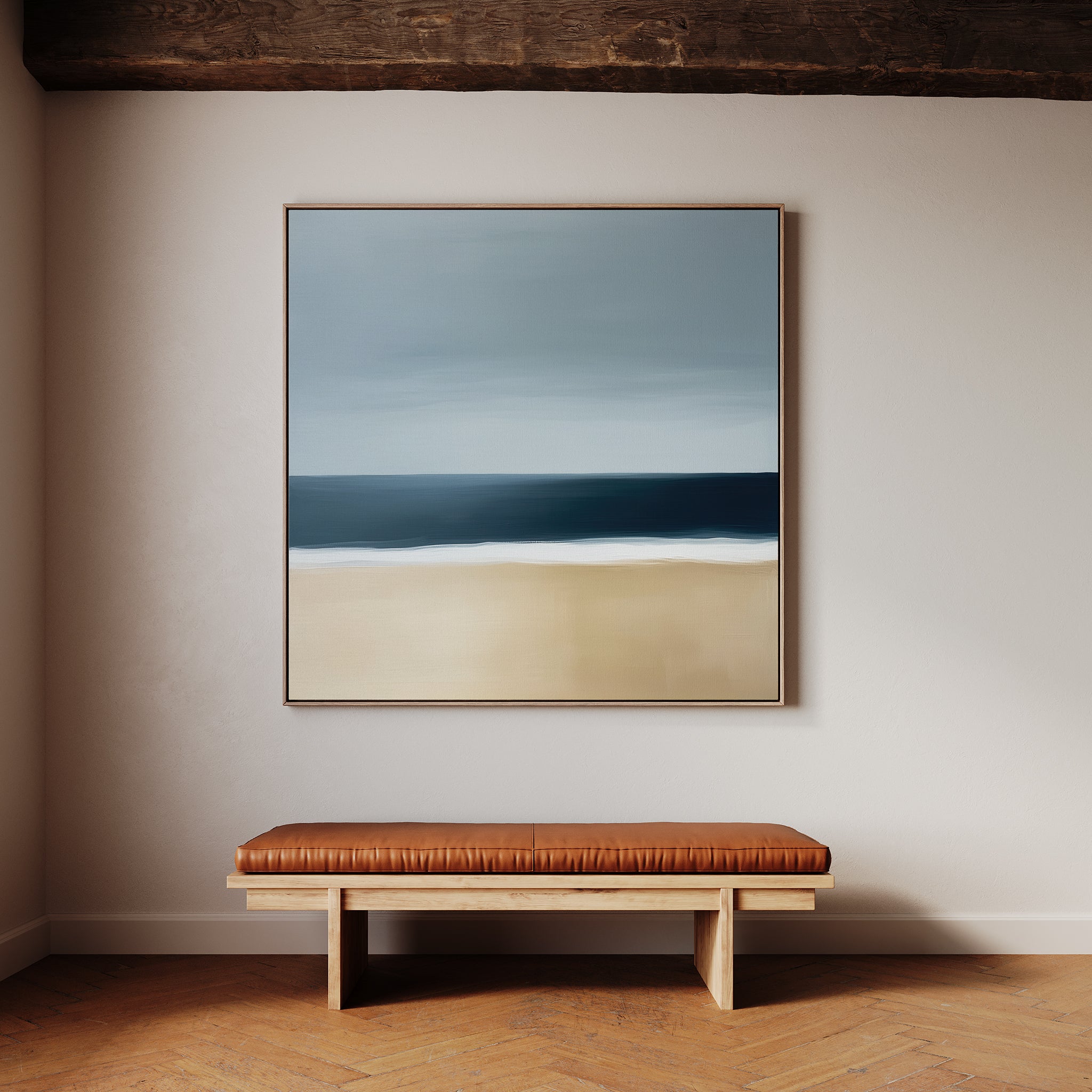 A minimalist interior showcases the Ocean Edge Canvas Art—a coastal beach scene—hung above a simple wooden bench with a brown leather cushion, all set against a light-colored wall and wooden floor.