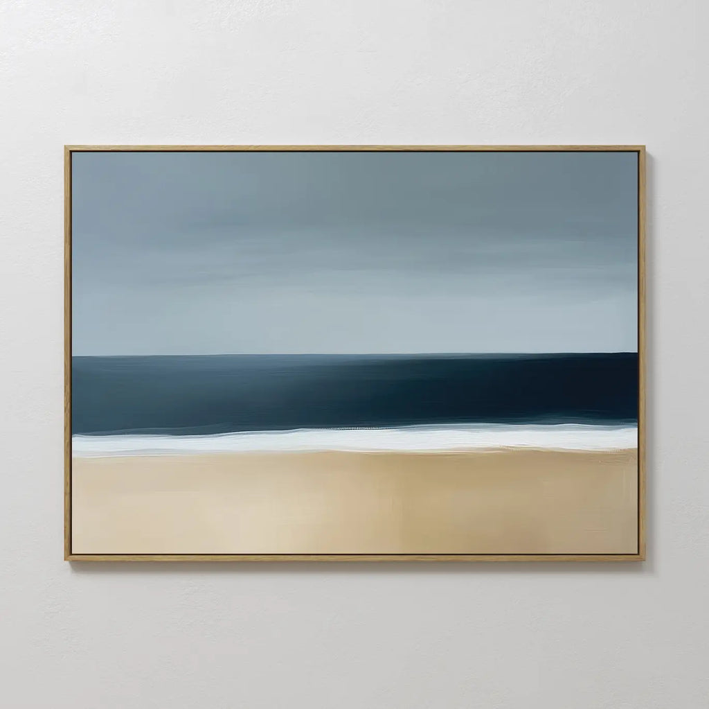 Ocean Edge Canvas Art – Horizontal features a minimalist seascape with a sandy beach, dark blue ocean, and an overcast gray sky. Framed in gold, this abstract coastal artwork adds elegance to any room.