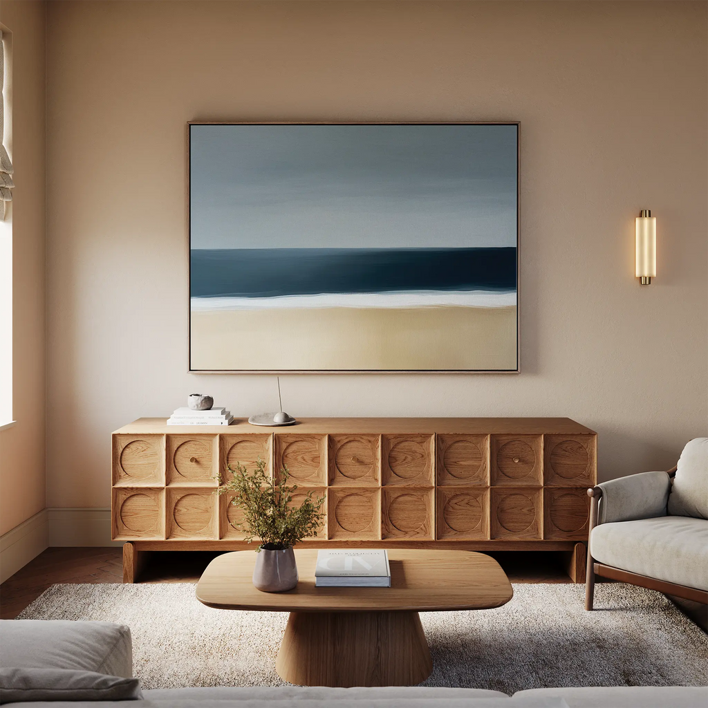 A modern living room with a wooden sideboard, low coffee table, and beige sofa. The Ocean Edge Canvas Art – Horizontal hangs above the sideboard, while a small plant rests on the coffee table.