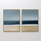 The Ocean Edge Set of 2 features framed abstract wall art with muted beige sand, deep blue water, and a gradient sky, creating a serene beach scene—perfect coastal decor for your living room.