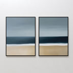 The Ocean Edge Set of 2 features minimalist abstract paintings of a blue sky, deep ocean, white surf, and sandy beach—ideal coastal wall art to elevate your living room decor on a plain white wall.