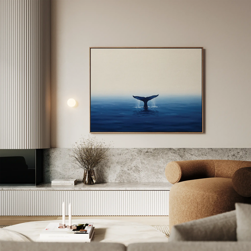 A modern living room showcases a neutral palette, a rounded beige armchair, a marble-topped console, and the Ocean Giant Canvas Art depicting a whales tail above blue water, adding to the serene ambiance above the console.