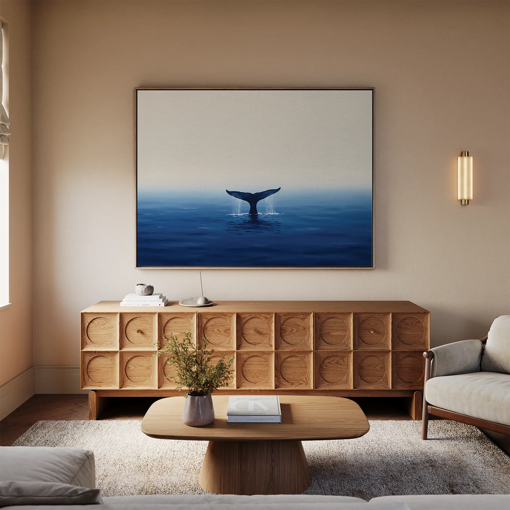 A cozy living room features a light sofa, wooden furniture, and the Ocean Giant Canvas Art above a textured wooden sideboard. A small table with books and a vase adds to the room’s relaxed coastal vibe.