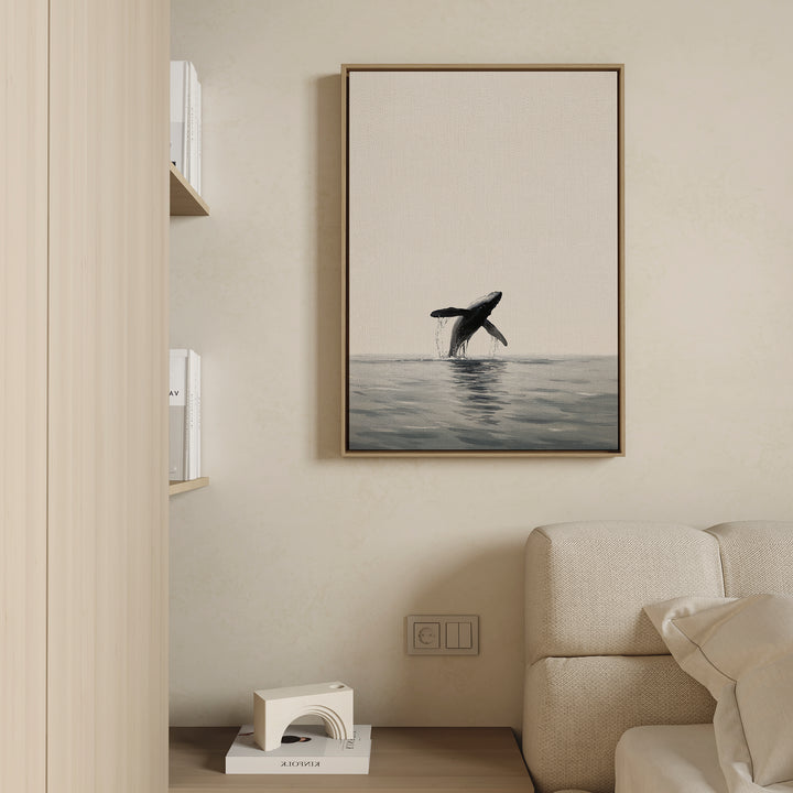 The Ocean Leap Canvas Art features a breaching whale above the ocean, displayed on a beige wall over a light sofa, with a bookshelf and decorative object nearby.