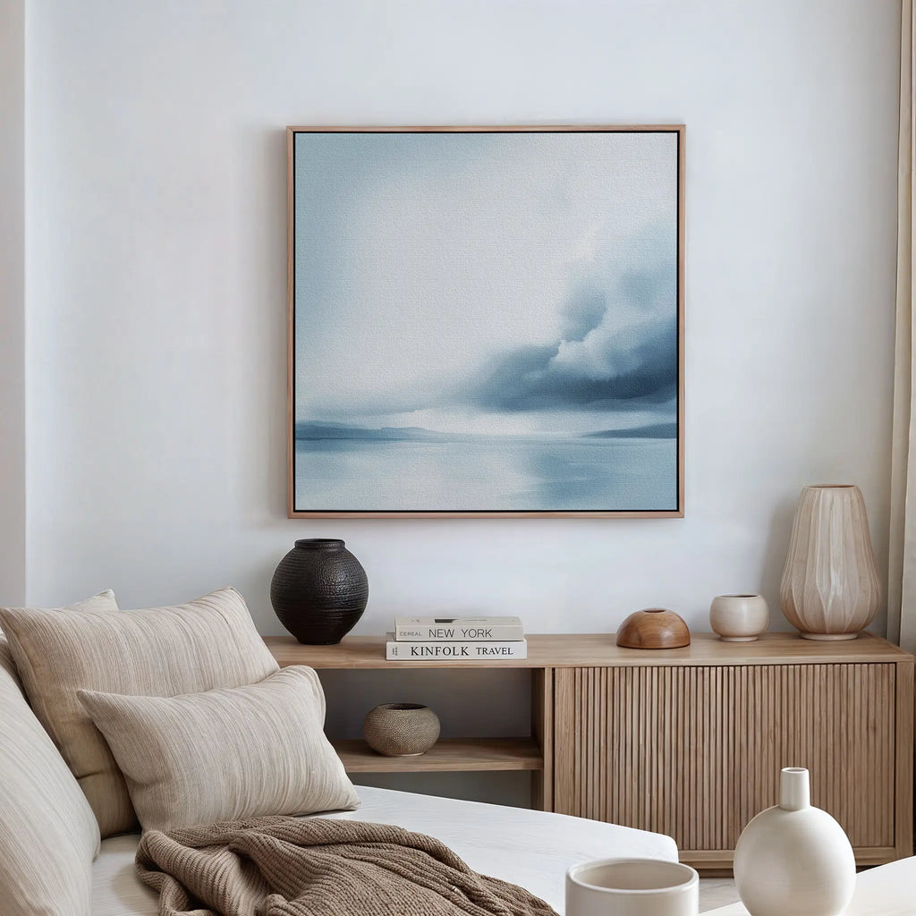 A minimalist living room with a beige sofa, cushions, a wooden sideboard, and the Oceanic Overcast Canvas Art on the white wall creates a calming atmosphere.