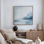 A minimalist living room with a beige sofa, cushions, a wooden sideboard, and the Oceanic Overcast Canvas Art on the white wall creates a calming atmosphere.
