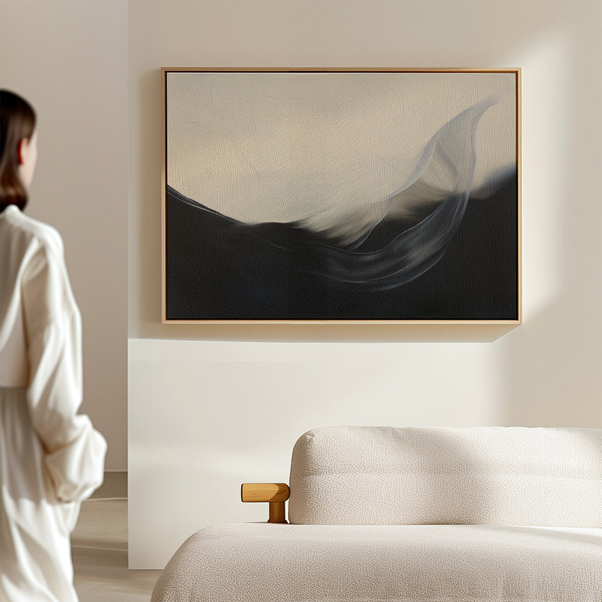 A person stands in a minimal, modern room with a light sofa and wooden armrest, admiring the Oceanic Pulse Abstract Canvas Art—an abstract painting with dark and light flowing shapes—hanging as stylish living room decor on a beige wall.
